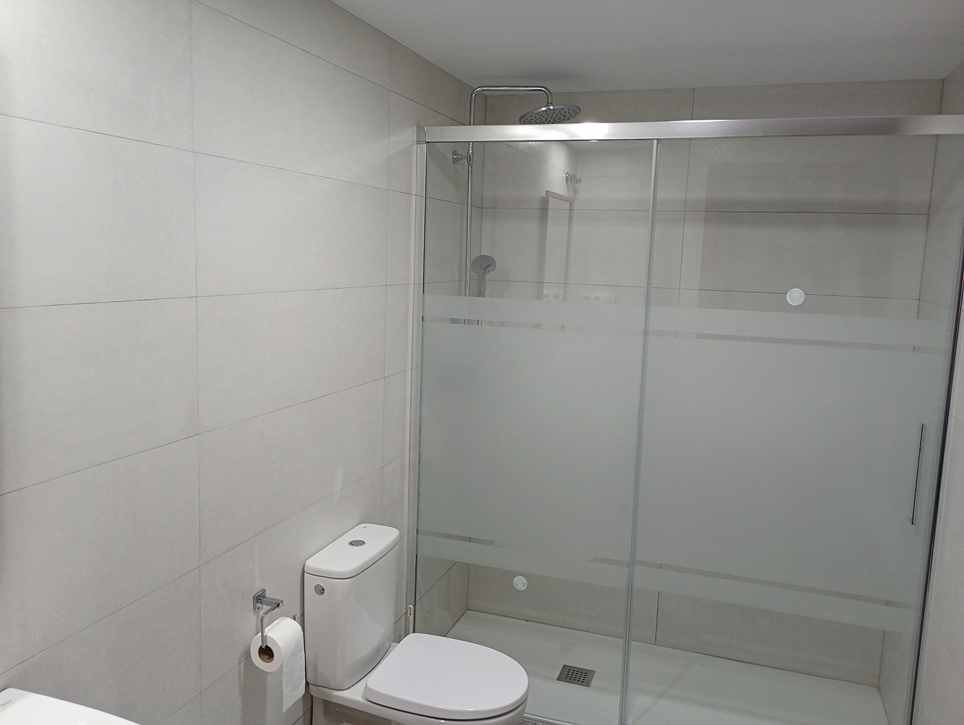 Ducha con mampara corredera y alicatado blanco en baño reformado