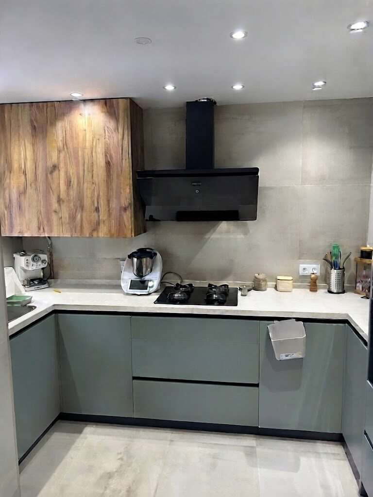 Cocina reformada en Sevilla moderna de diseño industrial con armarios en verde grisáceo, madera cálida y encimera de gran formato tipo cemento. Estilo funcional y elegante.
